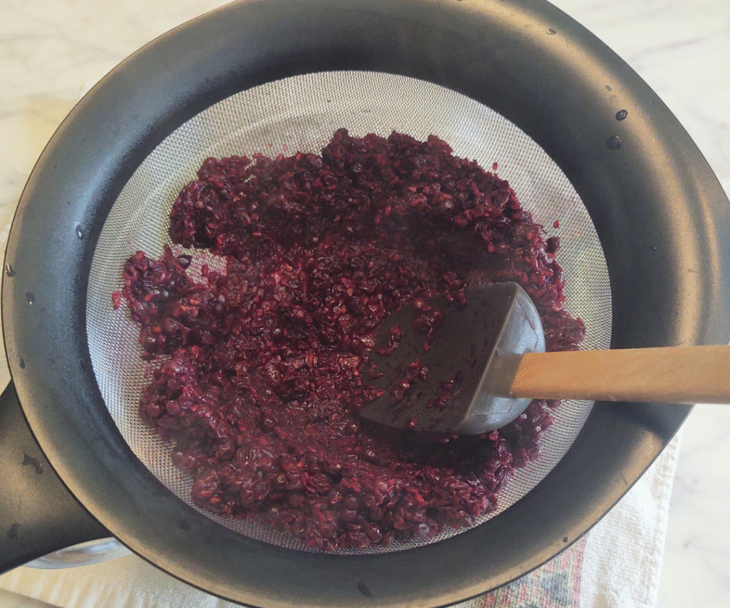 pressing elderberries through mesh strainer